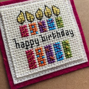 Peut inclure: Une carte blanche avec une bordure rouge et un motif de point de croix de cinq bougies avec des flammes et le texte "happy birthday".