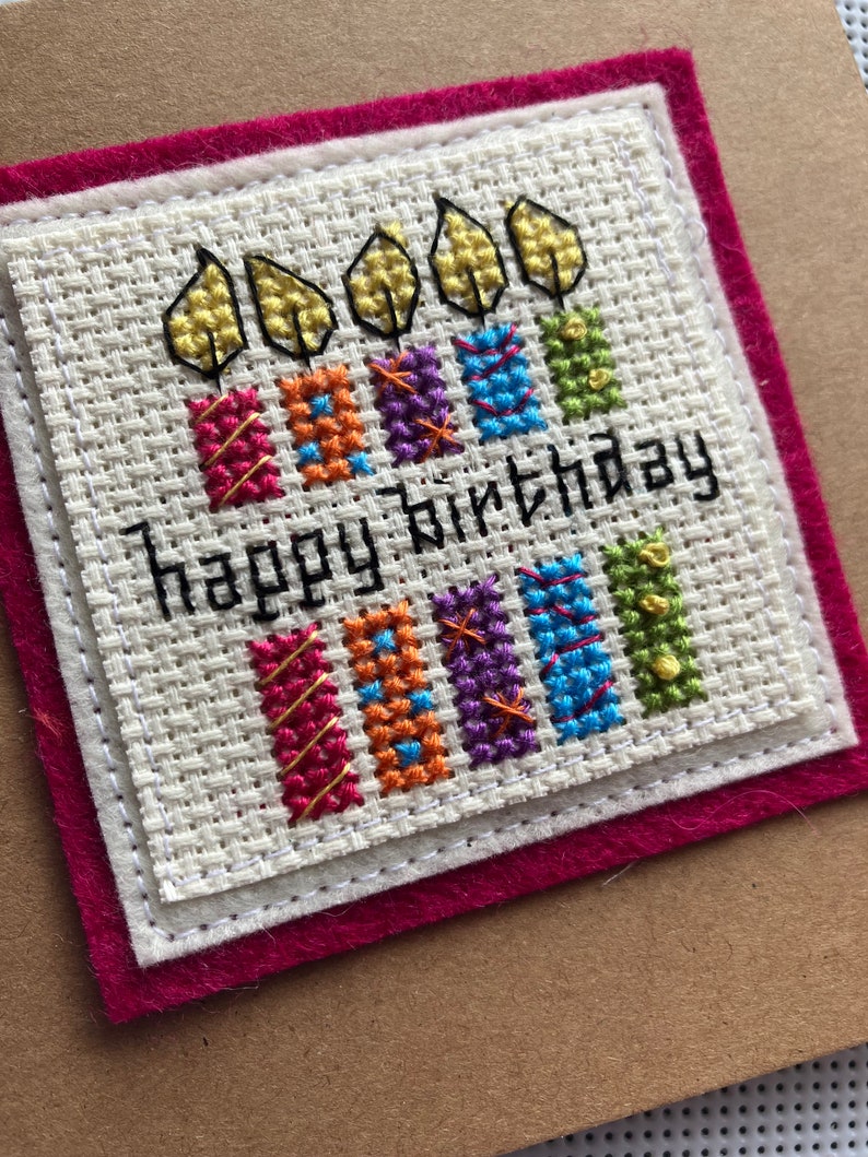 Peut inclure: Une carte blanche avec une bordure rouge et un motif de point de croix de cinq bougies avec des flammes et le texte "happy birthday".