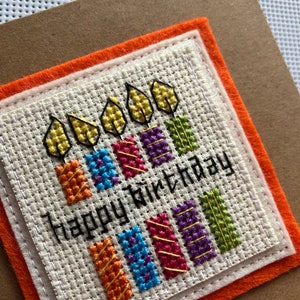 Peut inclure: Une carte faite &agrave; la main avec un motif de bougies color&eacute;es en point de croix et le texte "Joyeux anniversaire".