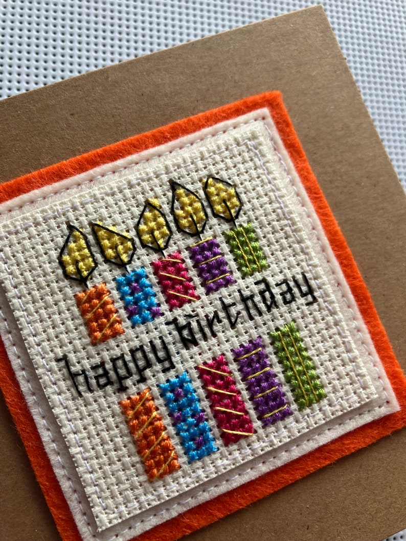 Peut inclure: Une carte faite &agrave; la main avec un motif de bougies color&eacute;es en point de croix et le texte "Joyeux anniversaire".