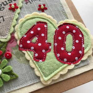 May include: Handmade birthday card with a felt heart featuring the number "40" in red polka dot fabric. The heart is on a light green background with a scalloped edge. Additional floral and button embellishments.