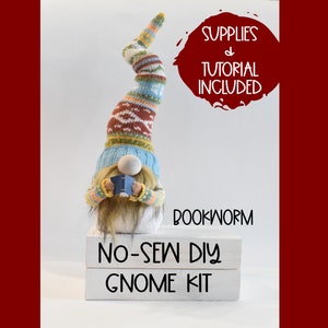 May include: A no-sew DIY gnome kit with a bookworm theme. The gnome is wearing a blue, yellow, and brown knitted hat and holding a blue book. The kit includes supplies and a tutorial.