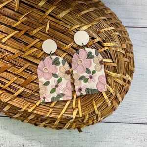 May include: A pair of pink and white floral arch-shaped earrings with white round tops.