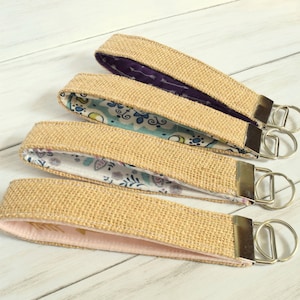 May include: Four keychains with a burlap exterior and different patterned fabric interiors. Each keychain has a silver key ring.