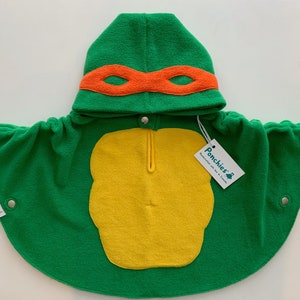 Op de afbeelding: Groene capuchon met een gele schildpad en een oranje masker. De cape is gemaakt van fleece en heeft een ritssluiting. Het label luidt "Ponchies-R Handgemaakt met liefde in Canada."