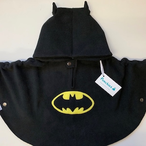 Op de afbeelding: Zwarte fleece-cape met capuchon met een geel Batman-logo en een label met de tekst "Ponchies".