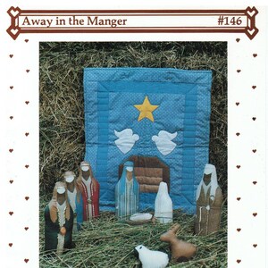 May include: A Christmas craft pattern depicting a nativity scene. The image shows figures of the holy family, angels, and animals, set against a blue backdrop with a star. The text "Away in the Manger" and "Country Threads" are visible.