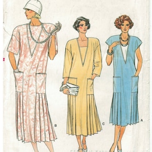 Può includere: Modello di cucito Vogue Patterns con tre abiti da donna. Gli abiti sono rosa, gialli e blu, ciascuno con scollo a V, tasche e gonna a pieghe. Il numero del modello è 9211, taglia 8.