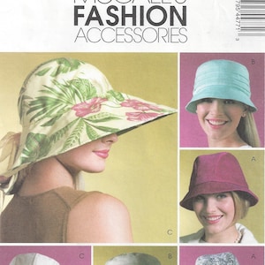 May include: A McCall's Fashion Accessories pattern showcasing several hat designs. The hats include a wide-brimmed sun hat with a floral print, a pleated turquoise cloche, and a burgundy fedora. The pattern also shows a white hat and a paisley print hat.