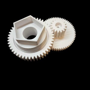 Peut inclure: Trois engrenages en plastique blanc de tailles différentes sont placés sur un fond noir. Le plus grand engrenage a une structure hexagonale centrale avec une ouverture circulaire. Les deux autres engrenages sont plus petits, l'un s'engrenant avec le plus grand.