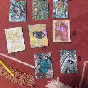 May include: A collection of eight small, rectangular art pieces. The artwork features various designs, including an octopus, floral patterns, a jellyfish, a bee, an eye, flowers, a bird, and a horse. The color palette includes blues, greens, and earth tones.