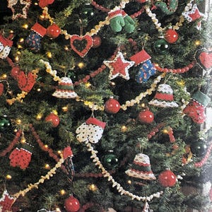 May include: A Christmas tree decorated with a variety of handmade ornaments. The tree features red, white, and green crocheted decorations, such as hearts, stars, bells, and mittens. Red and white beaded garland and red baubles are also visible.