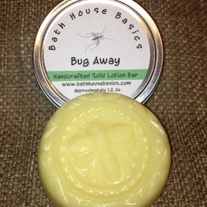 May include: A handcrafted solid lotion bar in a round shape with a bee design, next to a metal tin with the text "Bug Away" and "Bath House Basics". The lotion bar is approximately 1.2 oz.