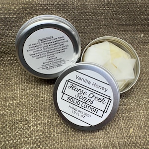 May include: A silver tin with a white label that reads "Vanilla Honey Horse Creek Soaps SOLID LOTION HAND POURED 1.2 FL OZ". The tin contains a white solid lotion bar.