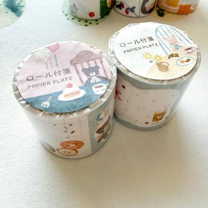May include: Two rolls of decorative washi tape with illustrated designs. One roll features a cake, teddy bear, and balloons. The other roll has a bunny, flowers, and a coffee cup. Each roll has Japanese text.