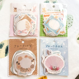 May include: Four packs of decorative stickers with pastel illustrations. Each pack features a different design, including a bunny, a plate setting, a teddy bear with cookies, and a seashell with an otter. The packaging includes Japanese text.