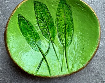 Puede incluir: Un plato de cerámica verde con borde dorado, con un diseño en relieve de tres hojas de salvia.