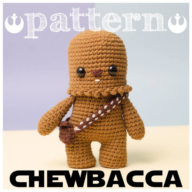 May include: A crocheted Chewbacca character from Star Wars. The character is brown with a white bandolier and a brown pouch. The character has a friendly face with black eyes and a brown nose.