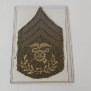 May include: A green military rank insignia with three gold chevrons and a gold embroidered eagle with crossed keys and a wreath.