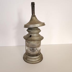 May include: A vintage metal and glass nautical lantern with a weathered silver finish. The lantern has a round glass lens and a tall, cylindrical body.