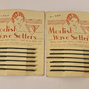 May include: Two vintage "Modish Wave Setters" hair styling kits. Each kit features a card with a woman's illustration and text. Each card holds several dark metal hair pins. The text reads "Keep your hair wavy...and at so little cost."
