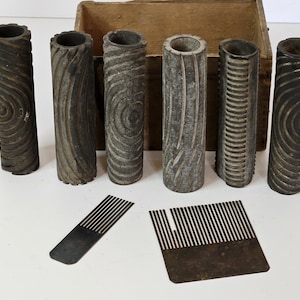 May include: A collection of vintage, weathered wood grain rollers and metal combs, likely for decorative or craft purposes. The rollers have various textured patterns, and the combs are rectangular with parallel teeth. A wooden box is in the background.