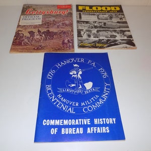 May include: Three vintage paperbacks, one blue with white text and a graphic of a man with a gun, one red with white text and a graphic of a battlefield, and one black and white with white text and a graphic of a flooded street.