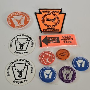 May include: A collection of eight patches and buttons featuring the Western Clinton Sportsmen's Association logo. The logo features a whitetail deer inside the outline of the state of Pennsylvania. The patches and buttons are in various colors, including orange, red, blue, and purple. The text "Western Clinton Sportsmen's Assn." and "Renovo, PA" are printed on the patches and buttons.