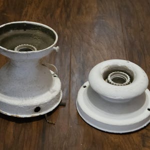 May include: Two white ceramic ceiling light fixture bases with a center hole for a light bulb.