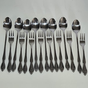 May include: A set of fourteen stainless steel utensils consisting of seven spoons and seven forks arranged in an alternating pattern. Each piece features a polished silver finish and a decorative embossed detail on the handle base.