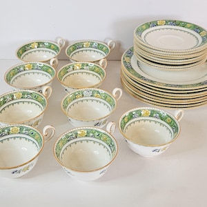 May include: A set of vintage teacups and saucers. The cups and saucers are white with a green, yellow, and blue floral design around the rims. The cups have gold handles and the saucers have a matching border. A classic tea set.