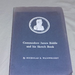 May include: A blue book with the title "Commodore James Biddle and his Sketch Book" by Nicholas B. Wainwright. The cover features a circular emblem with a portrait of a man and the text "The Congress of the U.S. to Capt. James Biddle for his Gallantry Good Conduct and Services."