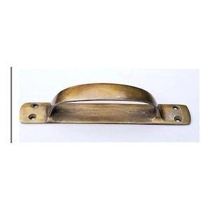 May include: A solid brass door handle with a curved top and two holes for mounting. The handle is a warm, aged brass color.