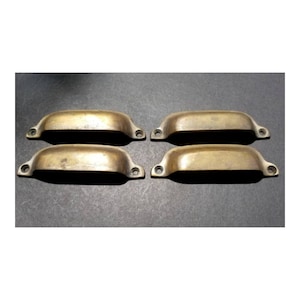 May include: Four antique brass cabinet pulls with a rounded rectangular shape. The pulls have a smooth, polished finish.