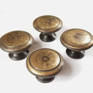 May include: Four antique brass cabinet knobs with a raised circular design and a dark brown base.