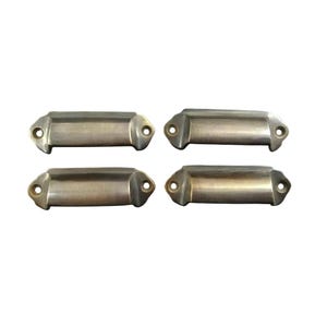 May include: Four antique brass cabinet pulls with rounded edges and a rectangular shape.