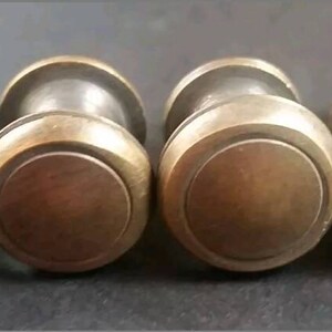 May include: Four antique brass cabinet knobs with a round, slightly raised, centre design. The knobs have a smooth, polished finish.