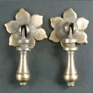 May include: Two brass drawer pulls with a flower design. Each pull has a round knob and a long, slender stem.
