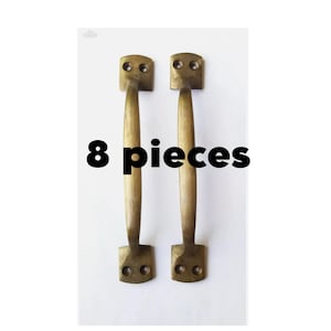 Peut inclure: Deux poignées de porte en laiton antique avec un dessus arrondi et un fond carré. Les poignées sont présentées sur un fond blanc. Le texte "8 pièces" est imprimé en noir sous les poignées.