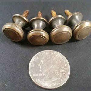 May include: Four brass knobs with screws, each with a raised circular design. The knobs are approximately the size of a UK 20 pence coin.