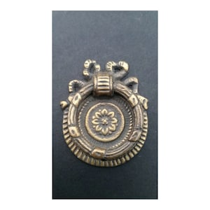 May include: A brass door pull with a decorative floral design and a ring handle. The pull has a distressed finish and a rustic look.