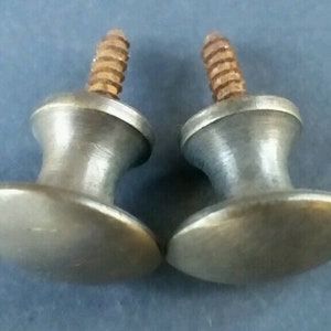May include: Two antique brass cabinet knobs with a round base and a screw. The knobs have a worn, aged finish.
