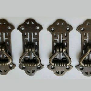 May include: Four antique brass drawer pulls with intricate designs and a ring handle. The pulls have a traditional Asian-inspired pattern.
