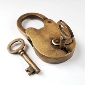 May include: A brass padlock with a key. The padlock is closed and the key is inserted in the lock. The padlock is a heart shape and the key is a simple design.