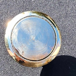 Op de afbeelding: Een gouden metalen flessenstop met een ronde, gladde bovenkant. De stop heeft een glanzend, reflecterend oppervlak.