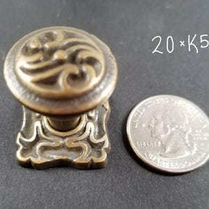 May include: Ornate brass-toned cabinet knob with a swirling pattern. The knob has a decorative base. A UK coin is next to the knob for size comparison. The text "20 x K5" is written in white.