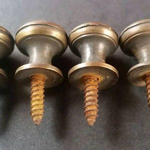 May include: Four antique brass cabinet knobs with screws. Each knob has a round top with a raised edge and a smooth, slightly textured surface.