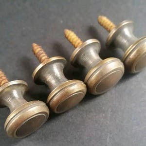 May include: Four antique brass cabinet knobs with a screw back. Each knob has a round, slightly domed top with a raised edge.