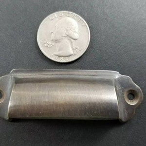 May include: A brushed nickel drawer pull with rounded edges and two screw holes. The pull is approximately 2 inches long and 1 inch wide.