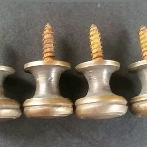May include: Four antique brass screw-in knobs with a rounded top and a single screw. The knobs are a light brass colour with a slightly aged patina.